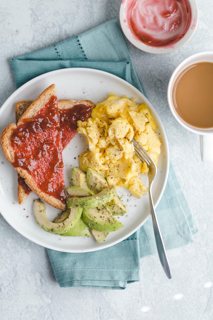 breakfast of scrambled eggs, toast with jam, avocado